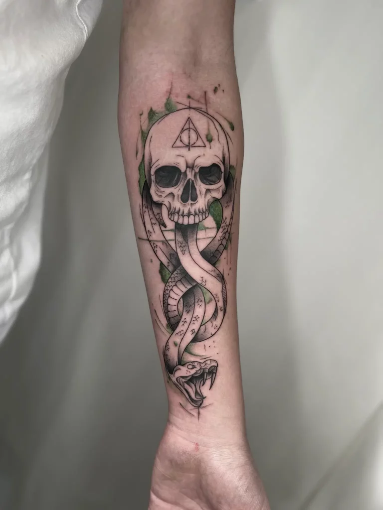 Tattoo auf dem Unterarm, dass einen Totenkopf mit Schlange zeigt und grüne Akzente hat